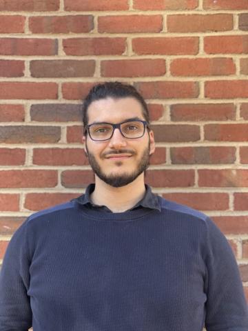 Photo of Dorian Demers in blue sweater with a brick wall behind him.